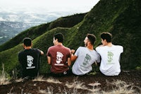 four men sitting on top of a mountain wearing t - shirts